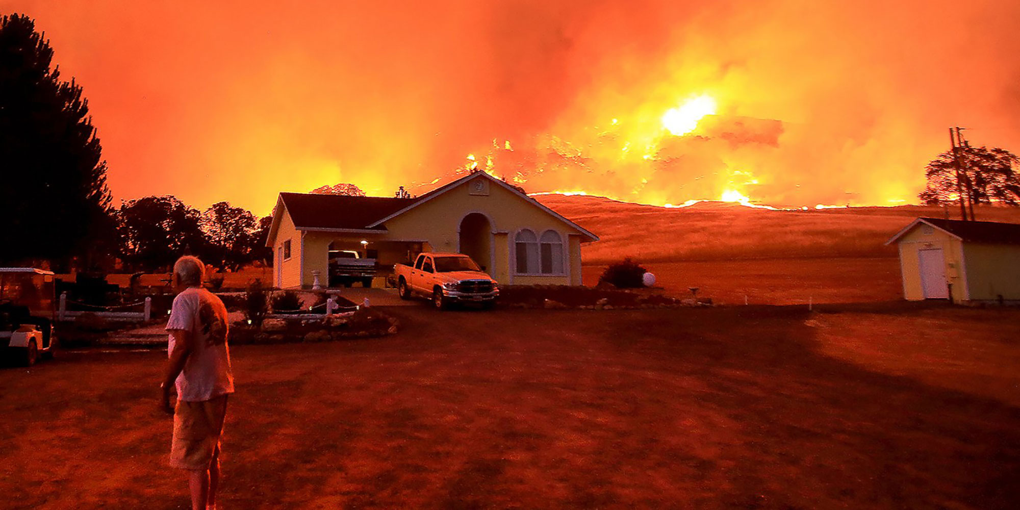 man in front of house with wildfire in surrounding landscape